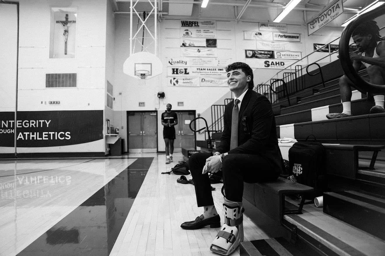 Black and white photo of Liam Besecker in a suit, smiling on the bleachers of a high school gym