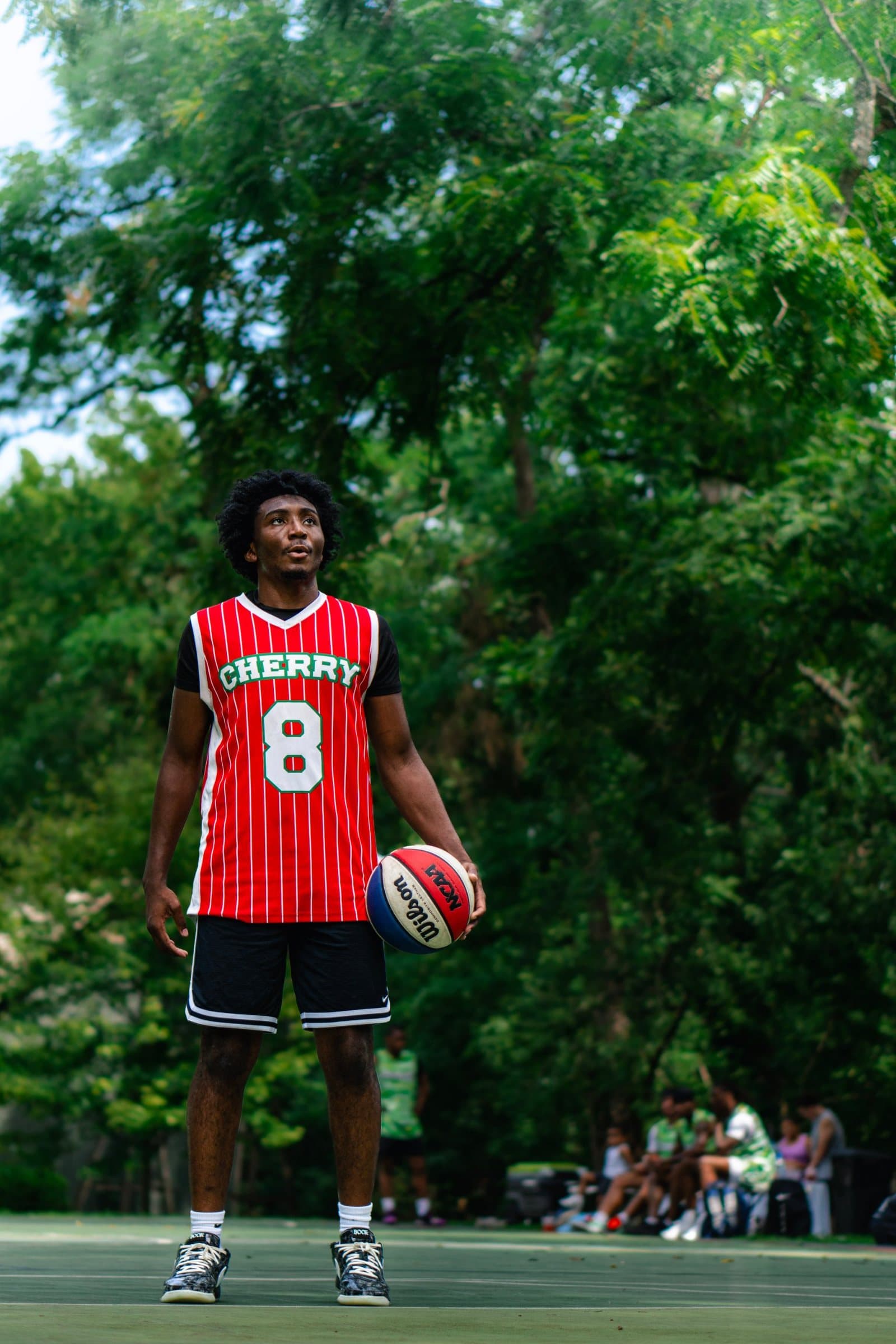 Player in a red pinstripe Cherry number 8 jersey holding a red, white and blue ball on an outdoor court