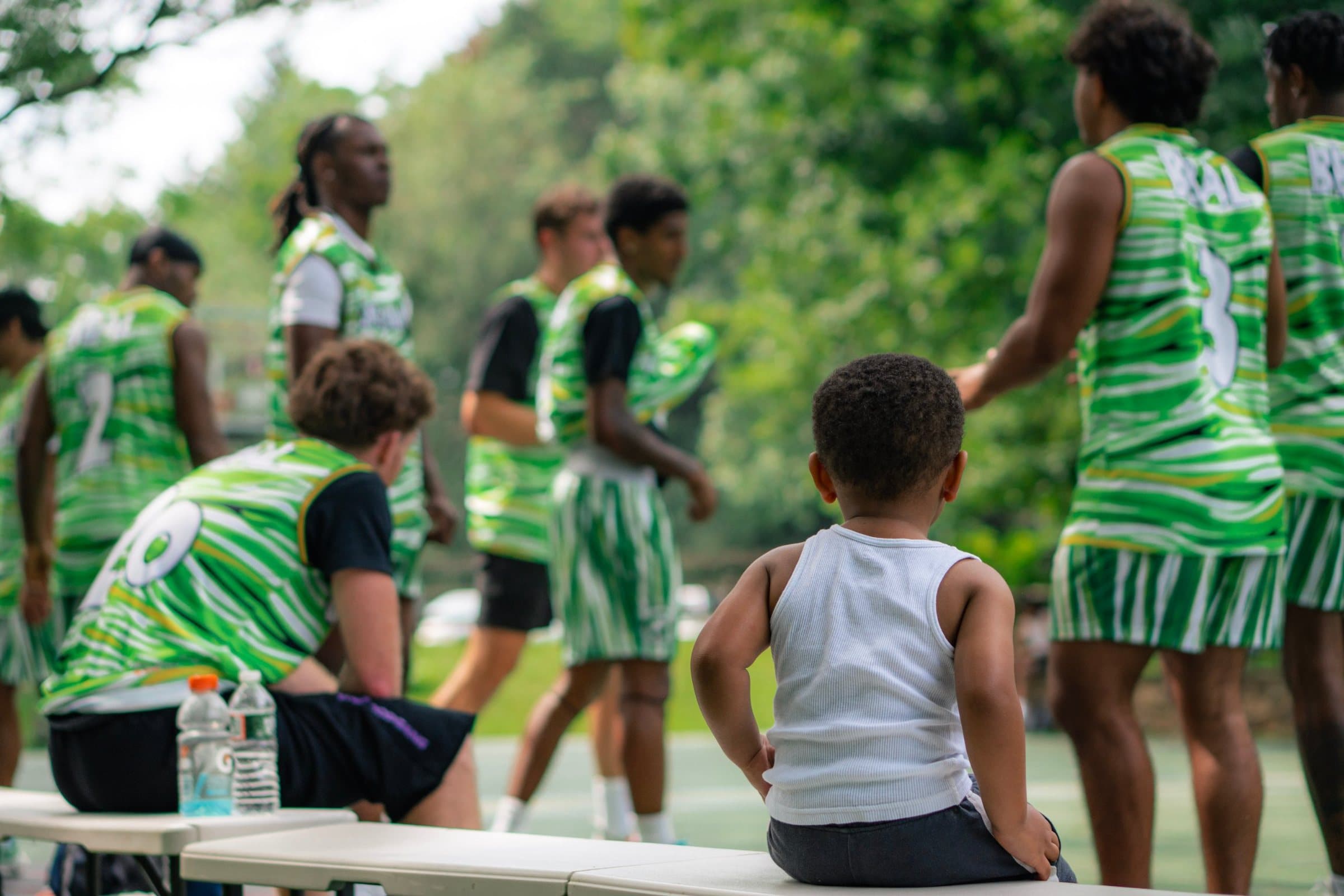A young kid on a bench watching a team in green BBAL jerseys