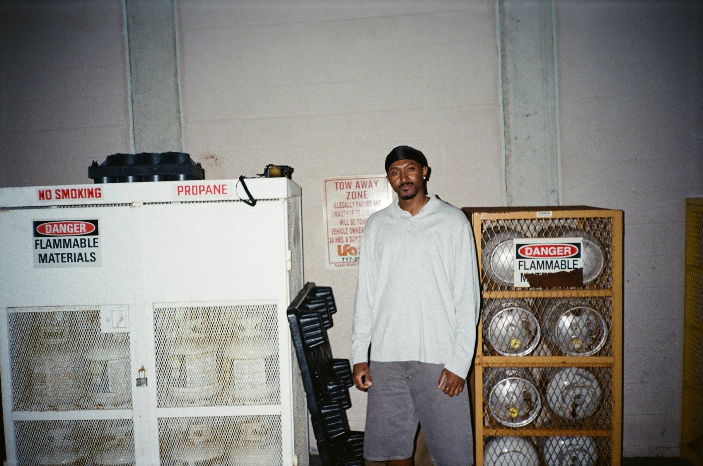 Man in a gray long-sleeve shirt and shorts standing between two propane tank cages