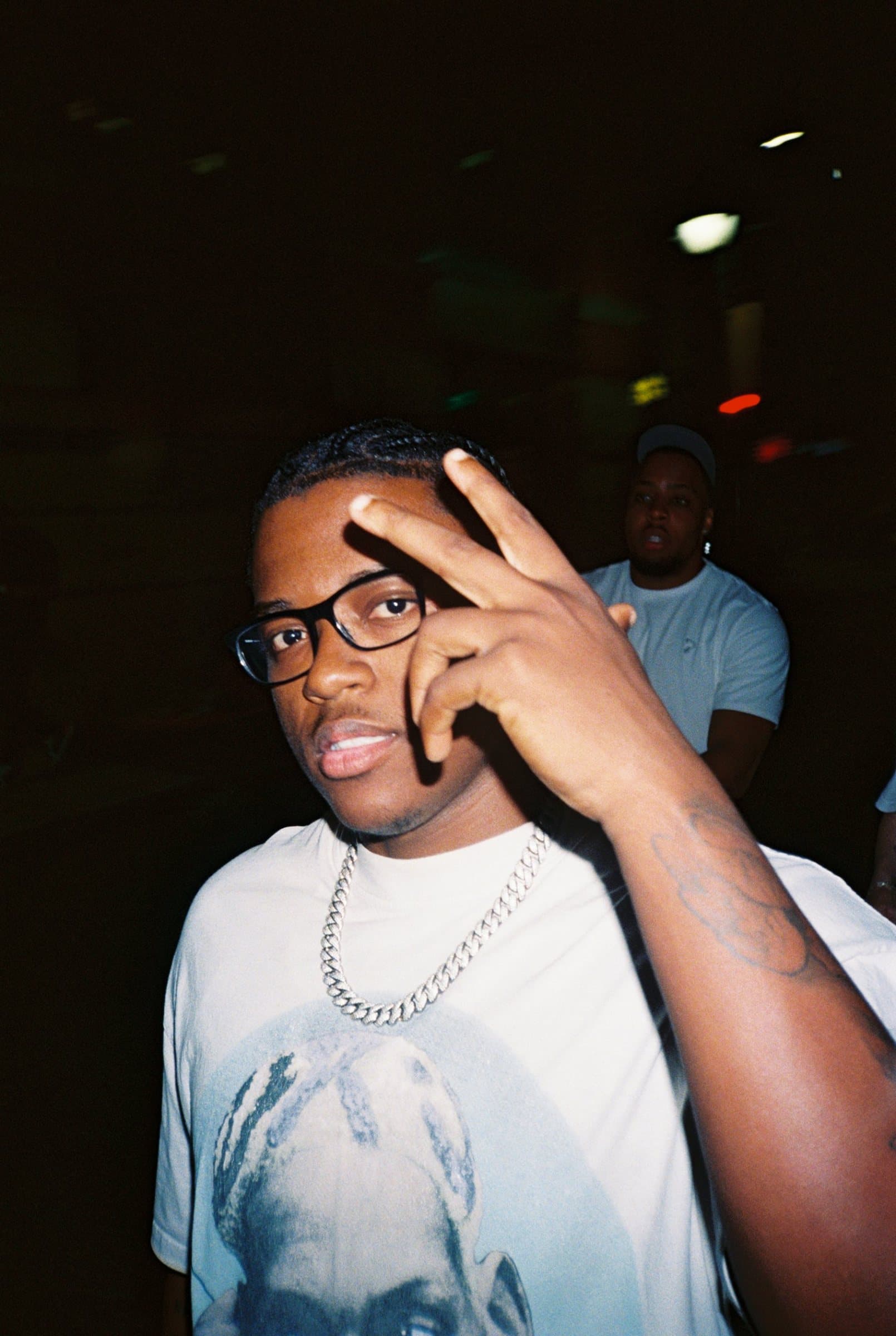Young man in glasses and a chain making a peace sign at night